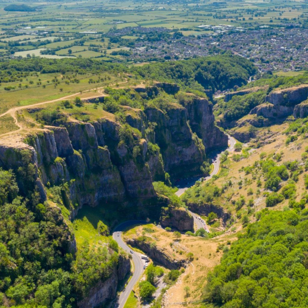 Picture showing Cheddar Gorge with a road running through and large cliffs on either side. Visiting is one of the things to do in England