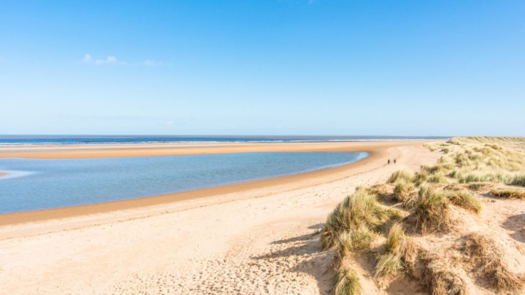 Vast expanse of beach with sea in the distance and sand dunes