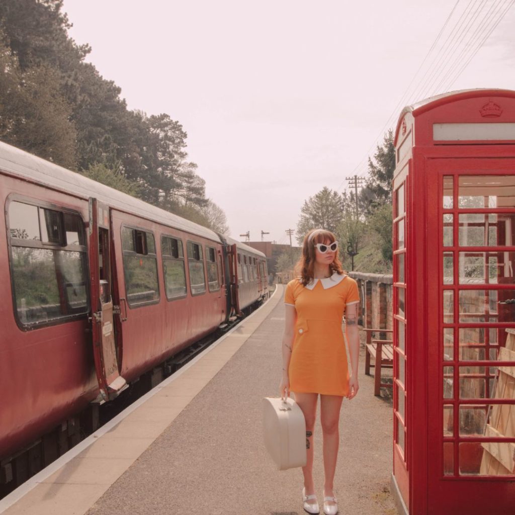 Girl stood by a phonebox and a vintage train