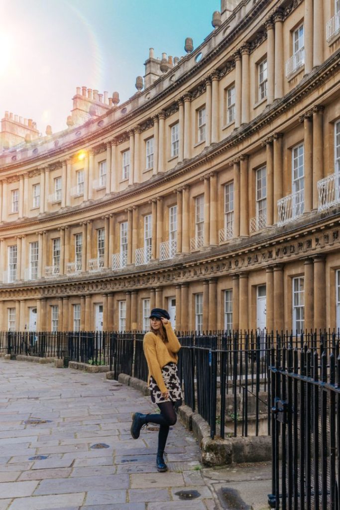 A girl in a cow skirt and yellow jumper with a hat on in front of some old houses